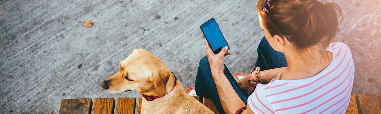 Woman holding a cell phone with her yellow dog sitting next to her.